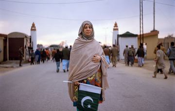 Woman in a beige saree holds a Pakistani flag, stood on the border between India and Pakistan