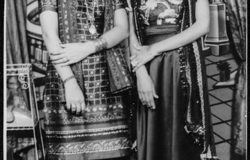 Two women in a black and white archive photo stand in saree smiling at the camera