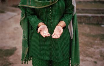 Woman's torso in a green and gold saree with her hands outstretched and palms facing up. Head is cut off the image,
