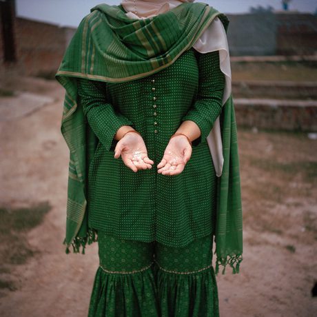 Woman's torso in a green and gold saree with her hands outstretched and palms facing up. Head is cut off the image,