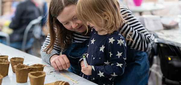 A woman and a young child are writing on a plant label with small seed pots around them