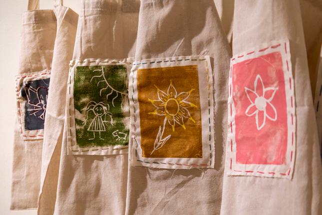 Beige tote bags hung up with different coloured material and screen printing with patterns on them