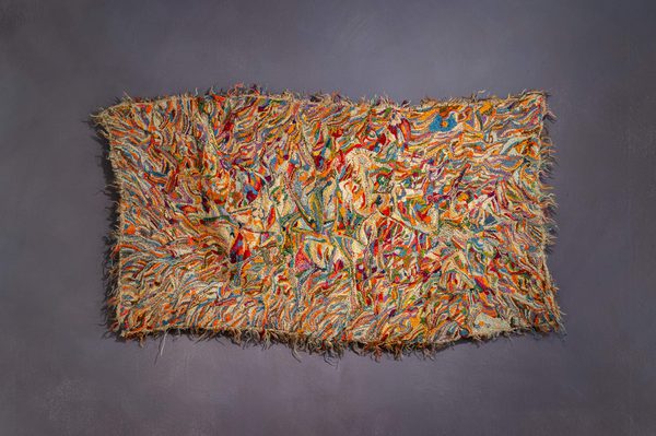 Multicoloured embroidery and woven work in a wonky rectangle on a dark blue/grey background