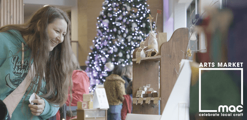 A woman is looking at a craft stall, with a twinkling Christmas tree in the background
