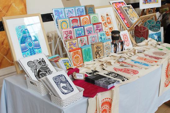 a table with various colourful cards, prints, tote bags laid out for purchase