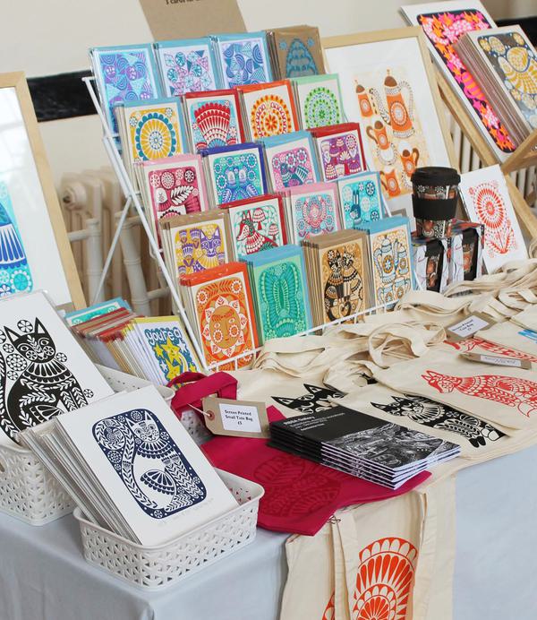 a table with various colourful cards, prints, tote bags laid out for purchase