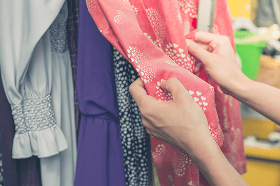 A close up of a rail of clothes, with hand reaching out to touch them