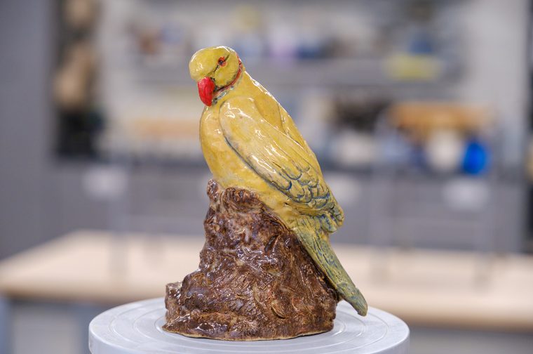 A yellow ceramic bird on a ceramic piece of wood