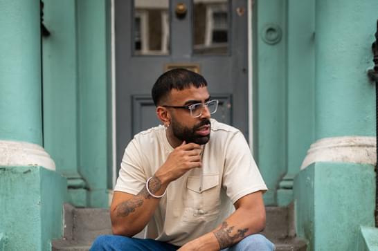 A person is sitting on concrete steps, holding a sewing machine between their legs with one hand. The walls behind them are a light blue.