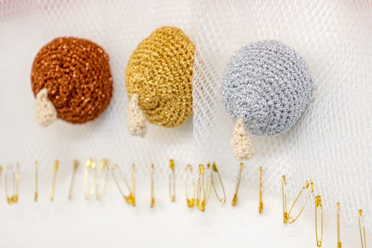 bronze, gold and silver stitched breasts made from wool on a mesh background held together with gold safety pins.