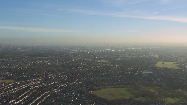 A shot from the sky overlooking a landscape, with green fields to the right and buildings to the right