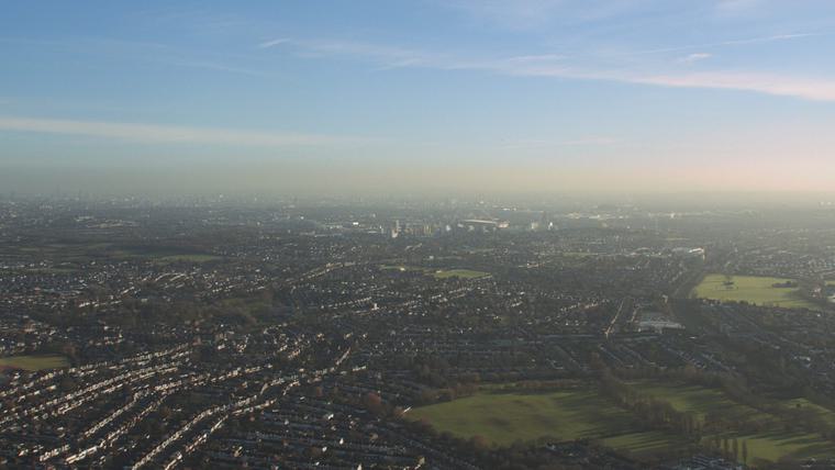 A shot from the sky overlooking a landscape, with green fields to the right and buildings to the right