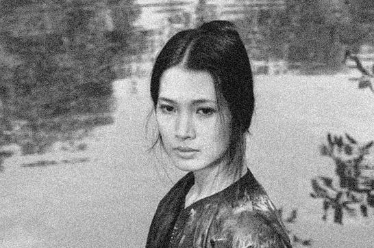 A young Vietnamese woman looks off camera in a blavkl and white image, standing in front of a lake.